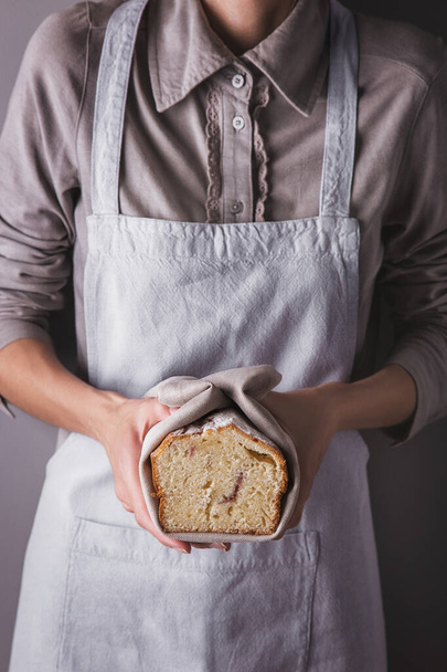 Girl in an apron and shirt holding a towel with a white sweet biscuit with powdered sugar and raspberries - Foto, afbeelding