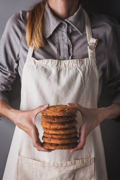 Girl in an apron and shirt holding several cookies with chocolate chips - Foto, afbeelding