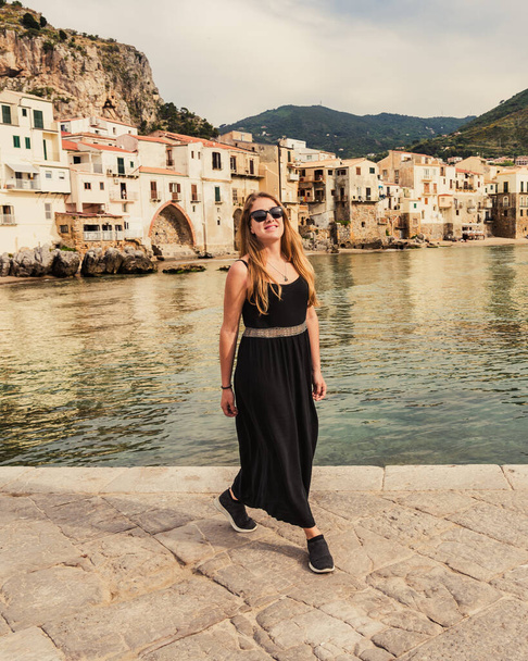 Чудова молода блондинка з сонцезахисними окулярами посміхається на пляжі середньовічного села Сицилійського острова (провінція Палермо, Італія) в похмурий весняний день.. - Фото, зображення