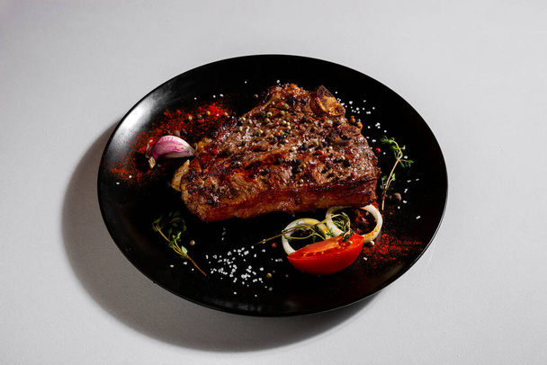 Fried pork steak with peppercorns, paprika, salt, onion, thyme, tomatoes and garlic in a plate on a white background - Foto, Bild