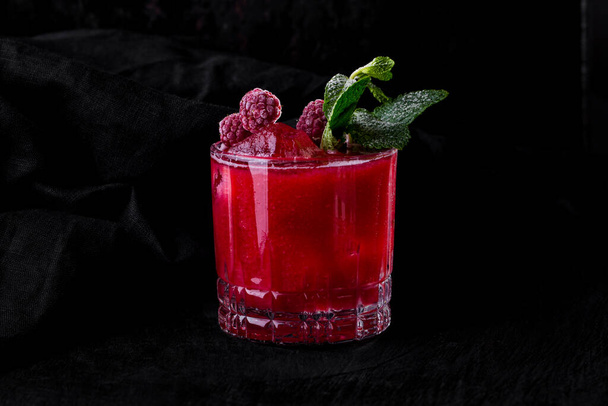 Cocktail with ice, raspberries and mint in a glass that stands on a wooden table on a dark fabric background - Φωτογραφία, εικόνα