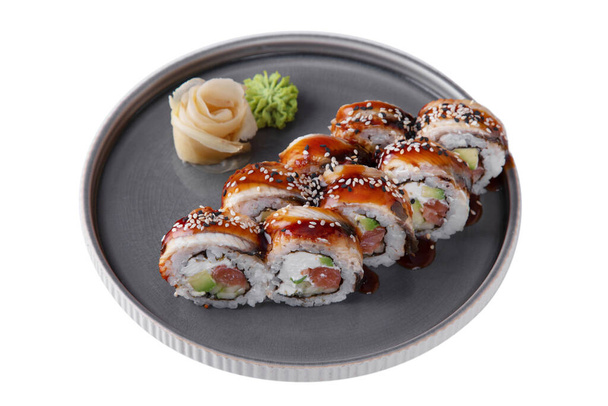 Roll with philadelphia cheese, salmon, sesame seeds, sauce, eel, αβοκάντο, rice, nori, wasabi and ginger in a dish on a white plate - Φωτογραφία, εικόνα