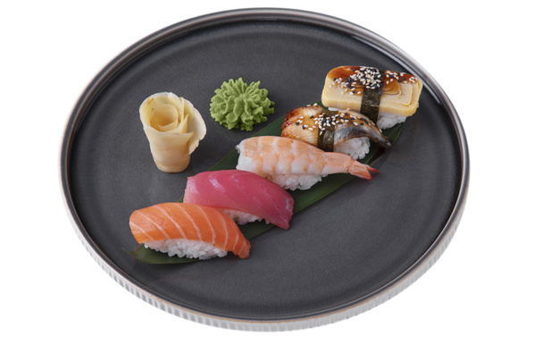 Sushi with salmon, shrimps, tuna, rice, eel, omelette, sesame seeds, nori on a banana leaf with wasabi, ginger on a platter on a white plate - 写真・画像