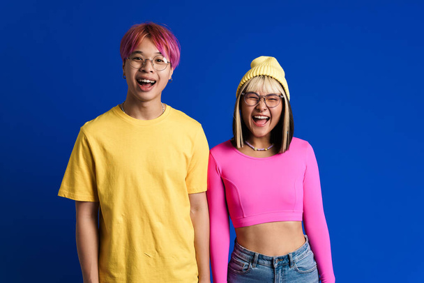 Asian teenagers in eyeglasses laughing and looking at camera isolated over blue wall - Foto, immagini