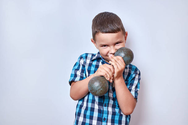 A boy tries to lift a heavy dumbbell. Fitness classes. - Zdjęcie, obraz