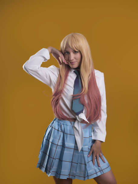 Charming young female model in white shirt and skirt with pink hair looking at camera while standing against brown background in light studio - 写真・画像