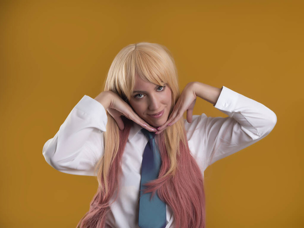 Charming female model with pink hair in white shirt and tie looking at camera with hands under chin on brown background in studio - Foto, immagini