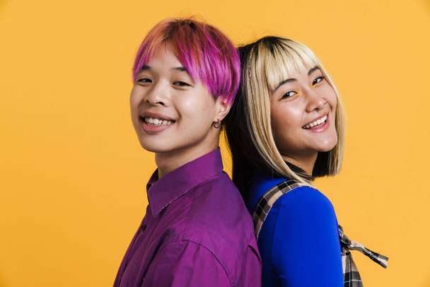 Asian couple with multicolored hair smiling while posing back to back isolated over yellow wall - Φωτογραφία, εικόνα