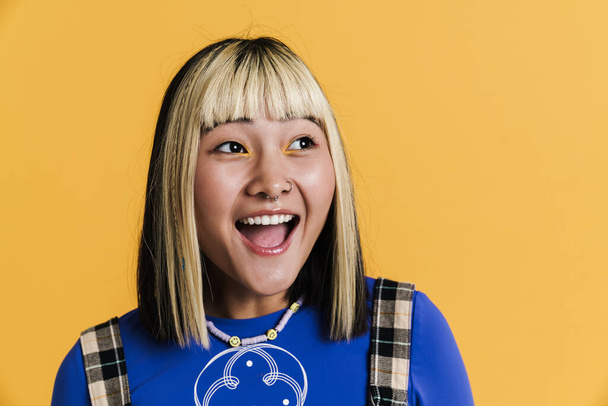 Asiática chica con piercing riendo y mirando a un lado aislado sobre amarillo pared - Foto, imagen