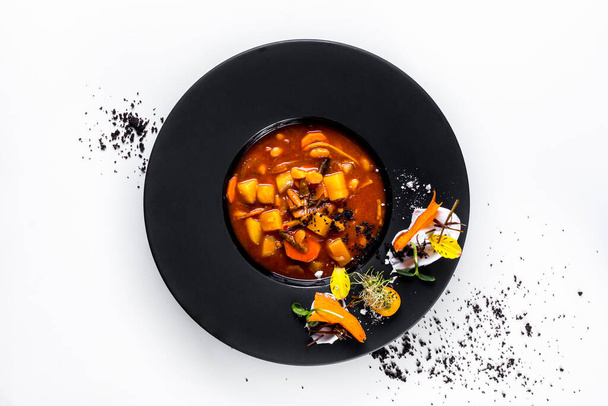 Soup with carrots, mung bean salad, sprouts, flower petals, kumquat, sauce, beans, potatoes and peppers in a plate on a white background - Photo, Image