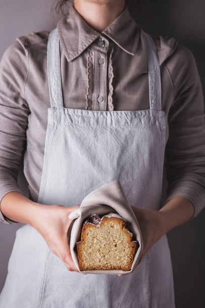Girl in an apron and shirt holding a towel with a sweet white cake with powdered sugar, lemon and honey - Foto, Bild