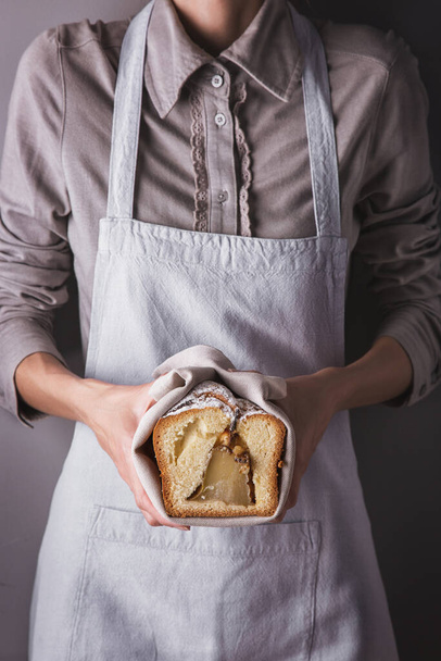 Girl in an apron and shirt holding a towel with a white sweet biscuit with powdered sugar and a pear - Foto, Bild
