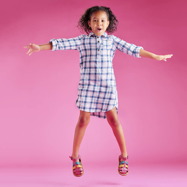 A pretty little mixed race girl with curly hair celebrating and dancing against a pink copyspace background in a studio. African child jumping and feeling free. - Фото, изображение