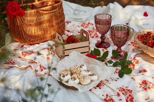 Kobiecy różowy letni piknik z obrusem, piankami, truskawkami, wiśnią, groszkiem i kieliszkami wina wśród różowych róż w parku. Romantyczny wieczór, podróże i uznanie chwili - Zdjęcie, obraz