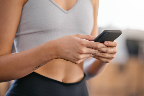 Closeup of one active caucasian woman texting on cellphone with while on break from exercise in a gym. Female athlete browsing fitness apps, social media and watching workout tutorials online. - Zdjęcie, obraz