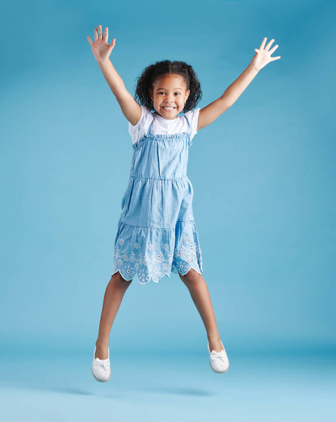 Счастливая молодая очаровательная маленькая латиноамериканка, прыгающая в воздух, изолированная на синем фоне. Забавная дошкольница выражает свое волнение и веселье. - Фото, изображение