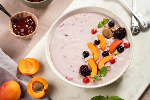 Traditional breakfast semolina porridge - purple creamy pudding with apricot slices, frozen berries, fresh mint, jelly on marble board - Φωτογραφία, εικόνα