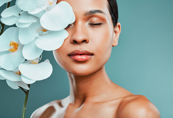 Studio portrait of an attractive young mixed race woman posing with a orchid against a green background. Latin female posing with a plant with her smooth soft skin. - Foto, Imagen