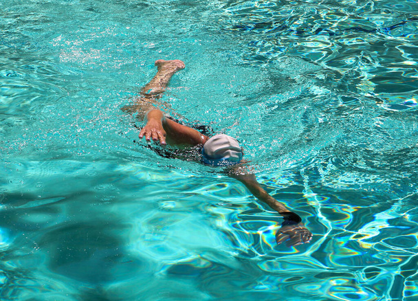 Front view of a women wearing a bathing cap swimming lapsin a hotel pool. - Foto, imagen