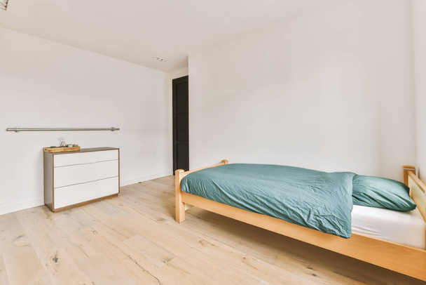 Удобная кровать без одеяла, возле окна и шкафа в светлой спальне - Фото, изображение