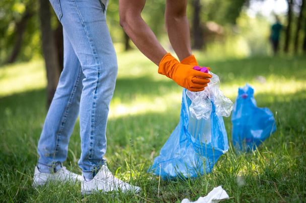 Cleaning, nature. Legs and hands of man collecting plastic garbage in bag in green park on sunny day no face - Foto, Imagen