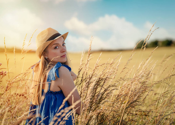 vrouw in jurk en hoed wandelen in een tarweveld in de zomer - Foto, afbeelding