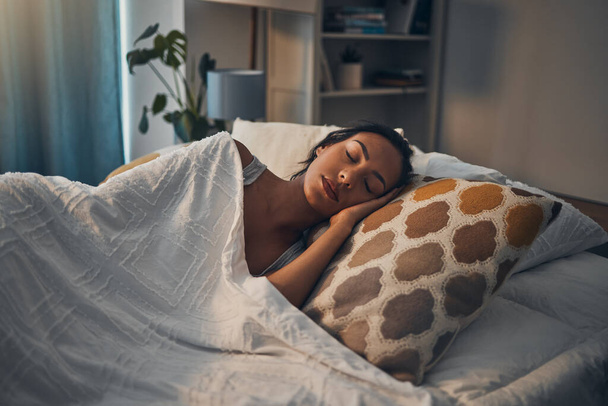 A beautiful young mixed race woman sleeping in a soft comfortable bed at home. One hispanic female feeling exhausted and resting in a comforting bed. - Photo, Image