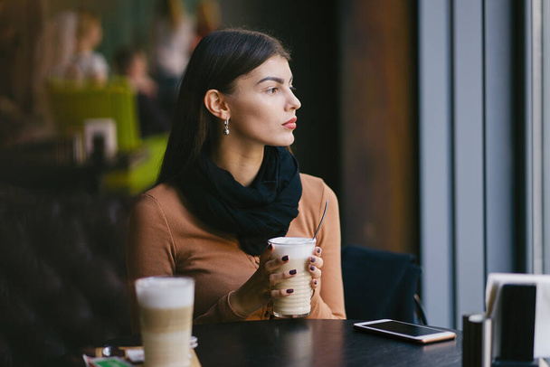 brunette girl using her phone while drinking coffee at a restaurant - Φωτογραφία, εικόνα