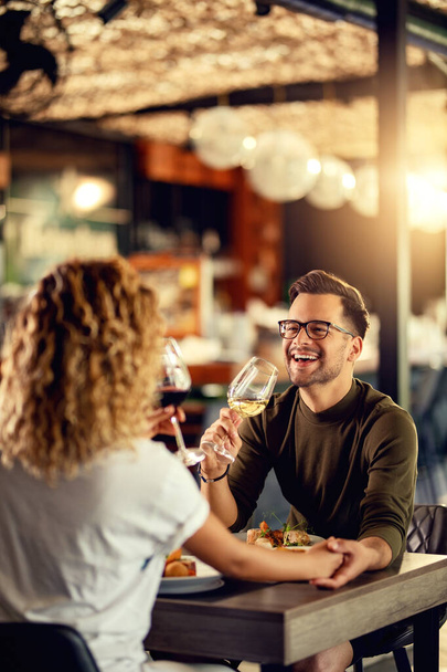 Молодая пара пьет вино и веселится во время обеда в баре. Фокус на человеке.  - Фото, изображение