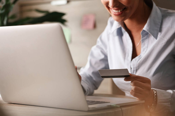 Крупним планом бізнес-леді купує в Інтернеті з кредитною карткою і ноутбуком в офісі
.  - Фото, зображення
