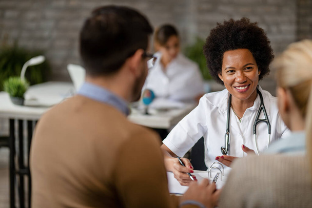 Happy black female doctor talking to a couple during consultations at clinic. - Foto, Imagem