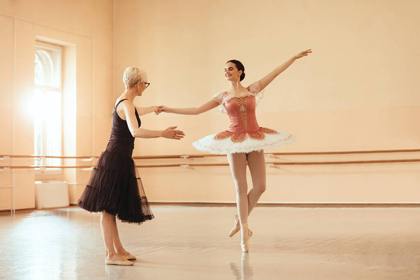 Young ballerina holding hand with her instructor while practicing in ballet studio.  - Photo, Image