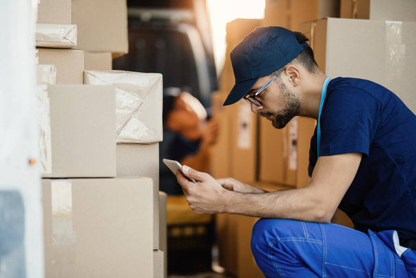 Delivery man working on touchpad while organizing packages for shipment in a van.  - 写真・画像