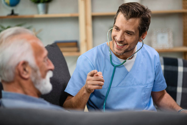Happy doctor gesturing while talking to a senior patient during a home visit.  - Photo, image