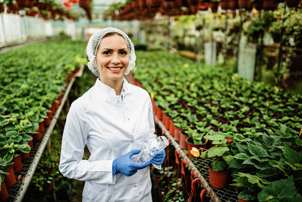 Portrait of smiling female scientist standing in a greenhouse and looking at camera.  - Zdjęcie, obraz