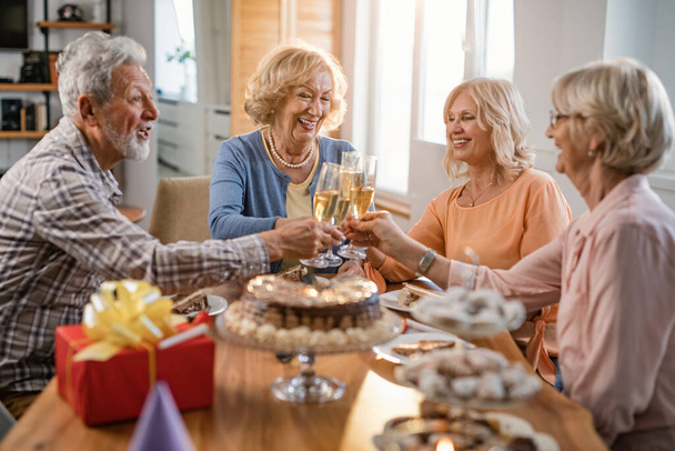 Счастливые зрелые друзья празднуют день рождения и пьют шампанское на домашней вечеринке.  - Фото, изображение