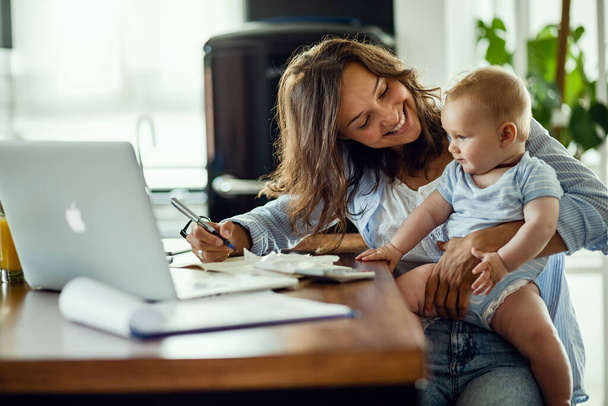 Young happy mother going through home finances and communicating with her baby son.  - Photo, image