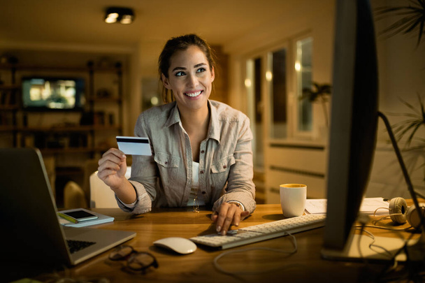 Молода щаслива жінка з покупками кредитних карток онлайн ввечері вдома
.  - Фото, зображення