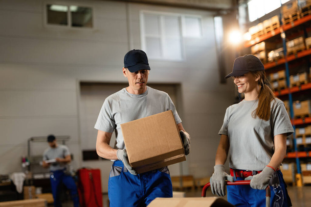 Happy woman and her male coworker working with cardboard boxes in a warehouse.  - Photo, image
