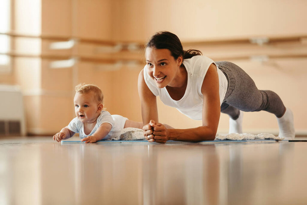 Athletic mother exercising in plank position while being with her baby on sports training. Copy space.  - Fotó, kép