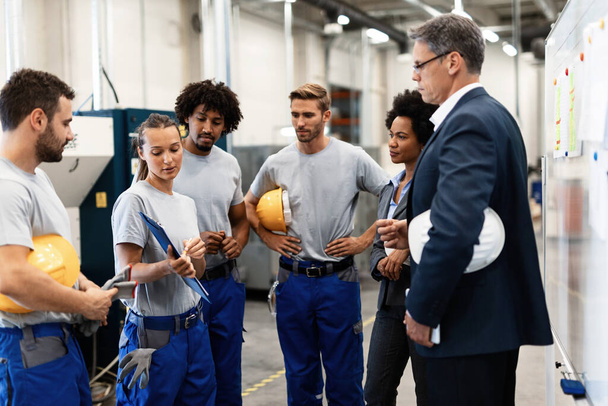 Group of workers having a meeting with company managers in a factory. Focus is on female worker is presenting development reports.  - Фото, изображение