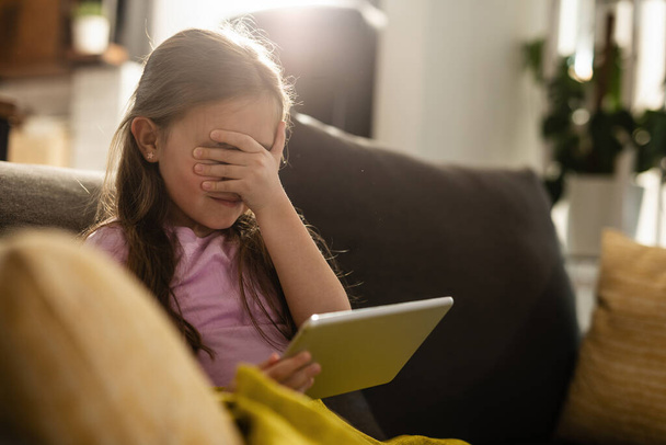 Φοβισμένο κοριτσάκι καλύπτει τα μάτια της, ενώ σερφάρετε στο Internet σε touchpad στο σπίτι.  - Φωτογραφία, εικόνα