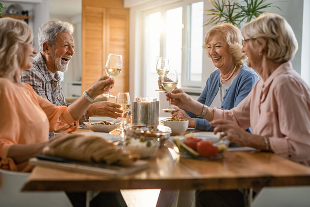 Група щасливих літніх людей розважається під час тостів з келихами під час обіду вдома
.  - Фото, зображення