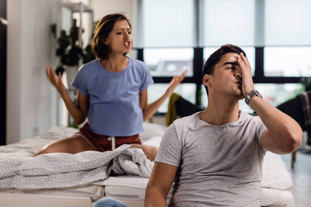 Young man feeling stressed out and having a headache while his girlfriend is arguing with him in the bedroom.  - Fotó, kép