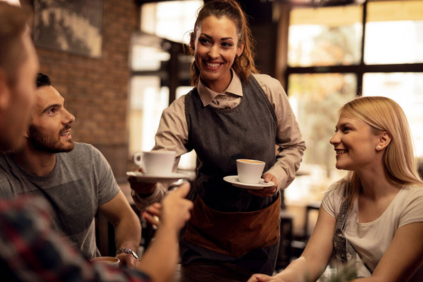 Χαρούμενη σερβιτόρα που σερβίρει καφέ σε μια ομάδα ανθρώπων σε ένα καφέ.  - Φωτογραφία, εικόνα