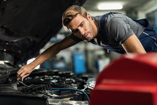 Young mechanic working on air conditioning system of a car in auto repair shop.  - Foto, Bild