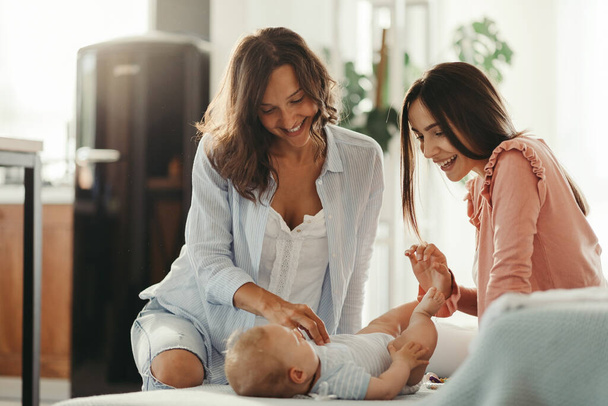 Female couple enjoying while playing with their baby boy at home.  - Foto, Bild