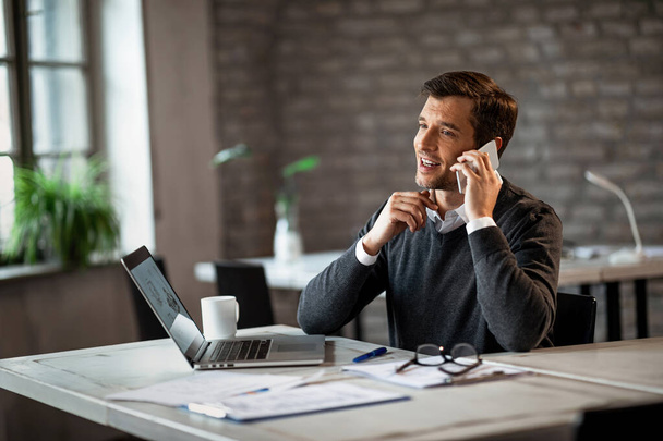 Счастливый бизнесмен сидит за своим столом в офисе и разговаривает по мобильному телефону.   - Фото, изображение
