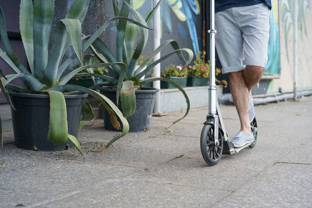 Close up man ride scooter with big wheels having a ride on the streets or park after work outdoors with agave plants on background. No face visible. Focus on front wheel with handle.  - Fotografie, Obrázek