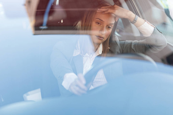 Νεαρή επιχειρηματίας αισθάνεται ενοχλημένη ενώ οδηγεί ένα αυτοκίνητο και να κολλήσει σε ένα μποτιλιάρισμα. Η θέα είναι μέσα από το γυαλί..  - Φωτογραφία, εικόνα